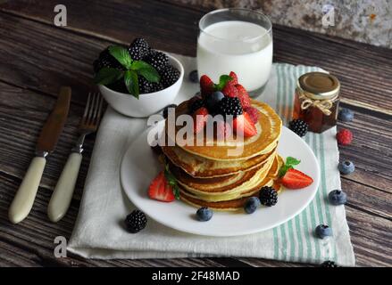 Crêpes avec fraises, mûres, miel et verre de lait sur une serviette de cuisine. Il reste des couverts. Banque D'Images