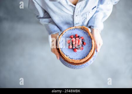Femme portant un cheesecake décoré de framboise et de myrtille, vue d'en haut Banque D'Images