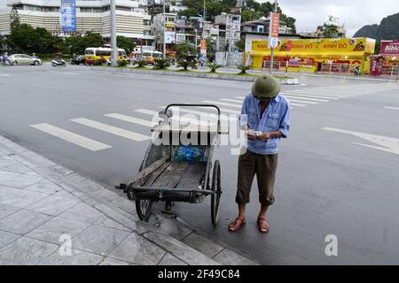 Ha long City, Vietnam - septembre 2015 : le chargeur compte de l'argent pour le travail dans la rue près de sa charrette en bois Banque D'Images