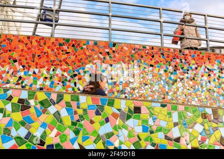 Düsseldorf, NRW, Allemagne, 19 mars 2021. Une femme en FFP2/KN95 masque le long du mur de mosaïque 'Rivertime', une installation d'art public par Hermann-Josef Kuhna à Dusseldorf, capitale de NRW. Les mesures de confinement devraient augmenter une fois de plus en Allemagne, le taux d'incidence sur 7 jours atteignant un seuil crucial de 100 000 habitants. Alors que Düsseldorf s'élève aujourd'hui relativement bien à 63, les chiffres de l'Allemagne ont augmenté à 95.6 Banque D'Images