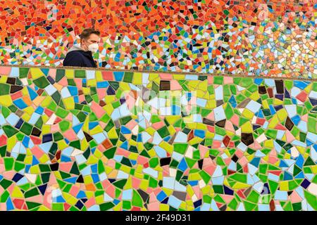 Düsseldorf, NRW, Allemagne, 19 mars 2021. Un homme en FFP2/KN95 masque de visage marche le long du mur de mosaïque 'Rivertime' par Hermann-Josef Kuhna, sur les rives du Rhin à Dusseldorf, capitale de NRW. Les mesures de confinement devraient augmenter une fois de plus en Allemagne, le taux d'incidence sur 7 jours atteignant un seuil crucial de 100 000 habitants. Alors que Düsseldorf s'élève aujourd'hui relativement bien à 63, les chiffres de l'Allemagne ont augmenté à 95.6 Banque D'Images