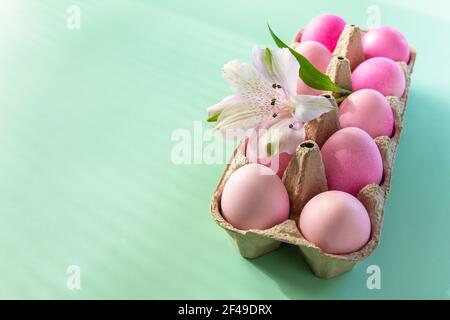 Concept de Pâques minimal. Ambiance printanière festive, décor naturel. Éléments de Pâques, boîte en papier avec œufs dans les couleurs roses et fleur sur fond vert pastel. Banque D'Images