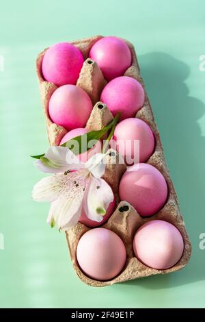 Lumière naturelle et ombre. Concept de Pâques minimal. Éléments de Pâques, boîte en papier avec œufs dans les couleurs roses et fleur sur fond vert pastel. Banque D'Images