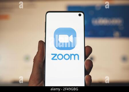 Homme tenant un smartphone avec le logo de l'application Zoom et un arrière-plan de site Web flou. Plate-forme de visioconférence et d'audioconférence Banque D'Images