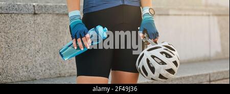 En-tête du site Web de Cropped shot de jeune femme sportive tenant un casque de vélo blanc et une bouteille d'eau tout en se tenant à l'extérieur, se préparer pour le vélo Banque D'Images