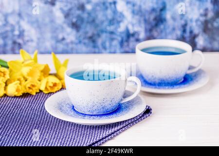 Deux tasses de thé bleu exquis et bouquet de jonquilles, thé papillon bleu tendance Banque D'Images