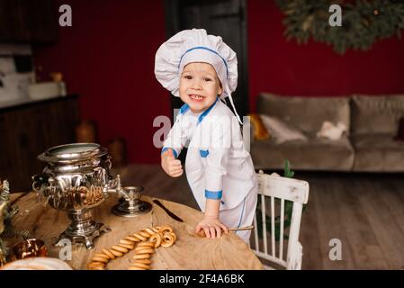 Concept de saine alimentation. Un petit garçon heureux cuisine dans la cuisine par une belle journée d'été. Lors d'un pique-nique, le boulanger mange du pain et des bagels dans un tablier blanc Banque D'Images