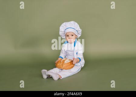 Concept de saine alimentation. Un petit garçon heureux cuisine dans la cuisine par une belle journée d'été. Lors d'un pique-nique, le boulanger mange du pain et des bagels dans un tablier blanc Banque D'Images