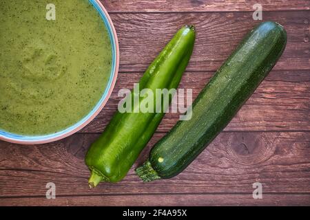 Soupe de detox de légumes frais à base de pois dans une assiette sur une table en bois brun avec concombres et poivre vert, vue de dessus avec espace pour le texte. Savoureux Banque D'Images