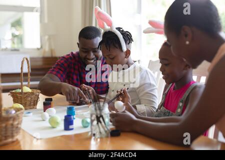 Parents afro-américains avec leur fils et leur fille portant des oreilles de lapin peinture d'œufs colorés Banque D'Images