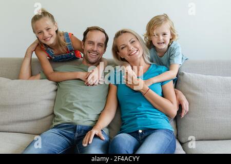 Portrait de parents caucasiens souriants assis sur un canapé avec leur fils et la fille les embrassant Banque D'Images