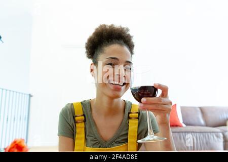 Femme de race mixte buvant un verre de vin et souriant à la maison Banque D'Images