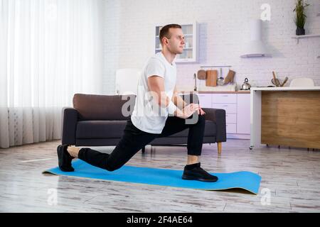 Homme sportif musclé dans un t-shirt faisant des exercices d'échauffement à la maison. Faire du sport à la maison pendant la période de quarantaine. Fitness à l'extérieur de la salle de gym Banque D'Images