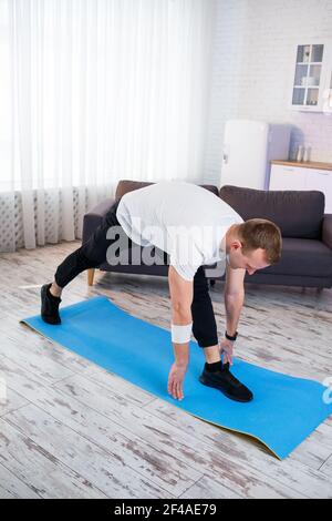 Homme sportif musclé dans un t-shirt faisant des exercices d'échauffement à la maison. Faire du sport à la maison pendant la période de quarantaine. Fitness à l'extérieur de la salle de gym Banque D'Images