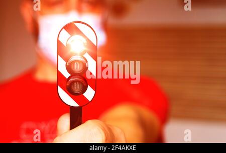Homme avec un masque chirurgical tenant un feu de circulation avec le feu rouge allumé, concept de zone rouge pendant le coronavirus Banque D'Images