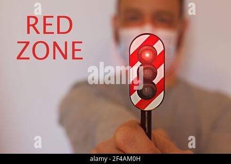 Homme avec un masque chirurgical tenant un feu de circulation avec le feu rouge allumé, concept de zone rouge pendant le coronavirus Banque D'Images