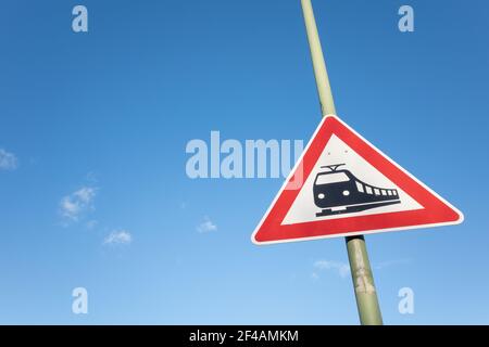 Le symbole noir du train sur le panneau rectangulaire rouge et blanc sur le poteau au croisement du chemin de fer contre le ciel bleu. Banque D'Images