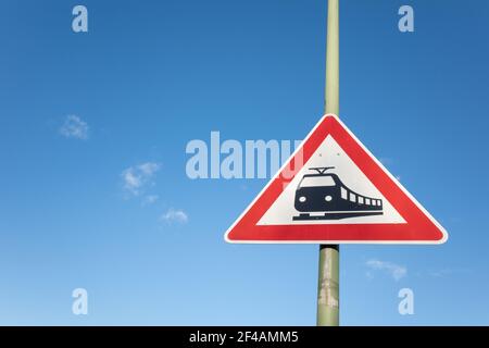 Le symbole noir du train sur le panneau rectangulaire rouge et blanc sur le poteau au croisement du chemin de fer contre le ciel bleu. Banque D'Images