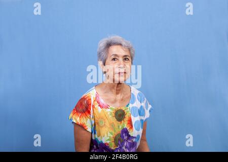Une femme âgée aux cheveux gris attrayante dans une chemise fleurie regardant l'appareil photo et sur un fond bleu. Banque D'Images