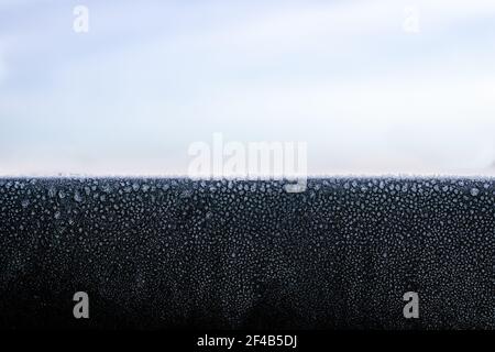 Toit noir clignotant en métal avec du givre ou des cristaux de glace tôt le matin, près du lever du soleil. Belle fine couche de glace sur une surface solide de congélation en dessous de la glace Banque D'Images