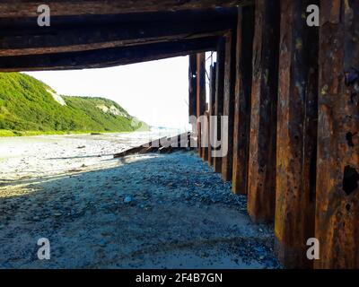 Plage sous un vieux pont rouillé. Des montagnes vertes au loin. Banque D'Images