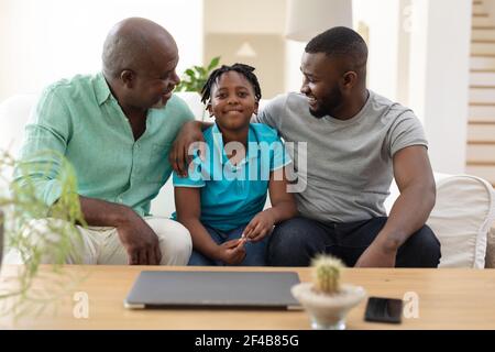 Grand-père afro-américain assis sur un canapé souriant avec un adulte fils et petit-fils Banque D'Images