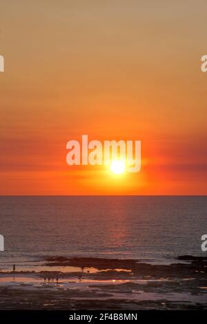 Vue lointaine des silhouettes de personnes profitant d'un coucher de soleil doré spectaculaire sur Cable Beach à marée basse, Broome, Australie-Occidentale. Banque D'Images