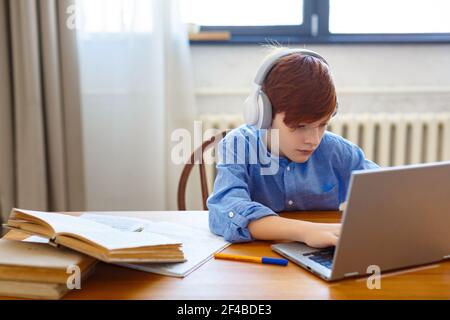 Un élève garçon pendant une leçon en ligne devant un moniteur d'ordinateur portable. Il écrit un message en ligne à l'enseignant. Concept d'apprentissage en ligne. Banque D'Images