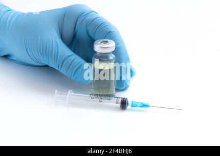 Main du médecin en gants bleus tenir le flacon avec un vaccin ou un médicament sur fond blanc. Concept d'étude de vaccination contre le coronavirus. Banque D'Images