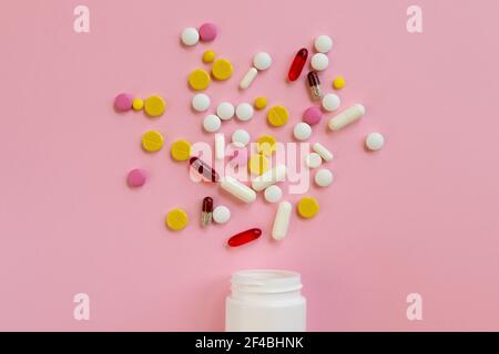 Assortiment de pilules et capsules médicales dispersées d'une bouteille en plastique blanc sur fond rose. Concept de traitement pour une personne malade. Vue de dessus. Plat Banque D'Images