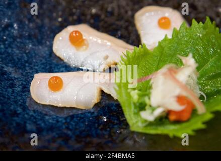 Poisson blanc Aburi coupé en tranches sur le dessus avec des œufs de saumon servis sur une assiette en céramique bleu foncé. Profitez de l'expérience Omakase au restaurant japonais Sushi. Banque D'Images