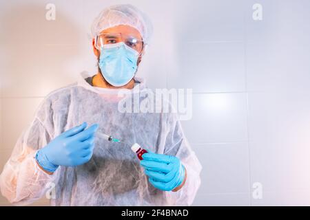 Un médecin masculin en costume de protection préparant une seringue pour la vaccination Banque D'Images