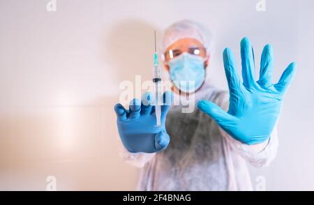 Un médecin de sexe masculin en costume de protection tenant une seringue avec le vaccin et le signe d'arrêt Banque D'Images