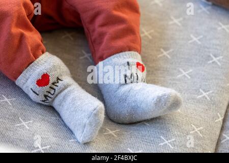 Un portrait des pieds d'un bébé avec des chaussettes grises et des pantalons, sur les chaussettes mignons le texte, j'aime maman, est écrit. L'enfant est allongé sur un oreiller gris. Banque D'Images