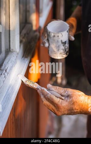 Homme senior peint des fenêtres en bois à l'aide d'un pinceau. Réparation de l'extérieur de la vieille maison. Banque D'Images