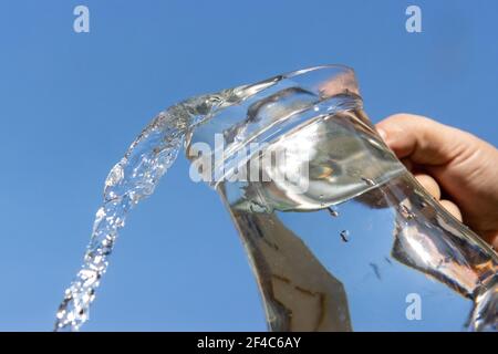 Une eau claire s'écoulant d'une verseuse en verre sur un fond bleu. Banque D'Images