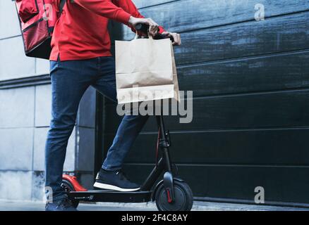 Cavalier homme livrant repas à la maison de clients avec scooter électrique - concept écologique de livraison rapide de nourriture - Focus sur les pantalons Banque D'Images