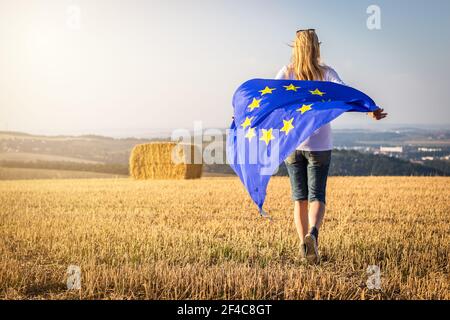 Femme qui court avec le drapeau de l'Union européenne à la campagne. Drapeau de l'UE en tant que symbole de liberté et de démocratie. Banque D'Images