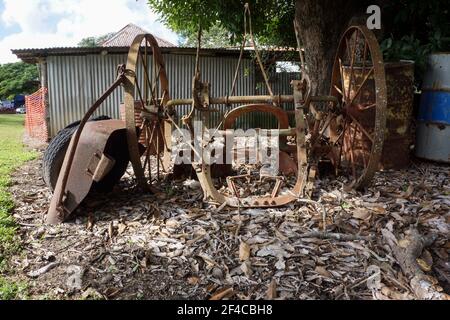 Vieux matériel agricole utilisé pour planter la canne à sucre dans les tropiques, laissé à la rouille sous un manguier derrière un hangar. Banque D'Images