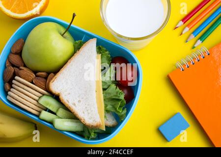 Déjeuner scolaire dans la boîte, lait dans le verre et carnet sur fond jaune.vue du dessus. Banque D'Images