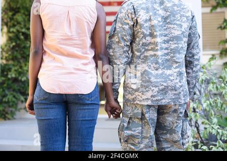 Mi-section d'un militaire et d'une femme afro-américains debout mains devant leur maison Banque D'Images