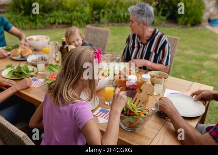 Une femme de race blanche parle avec une famille en train de manger ensemble jardin Banque D'Images