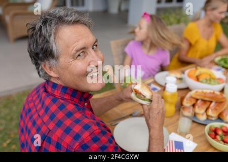 Un homme caucasien souriant tenant un hamburger avec un repas de famille ensemble dans le jardin Banque D'Images