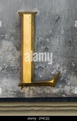 Lettre dorée historique L avec serifs sur un mur gris Banque D'Images