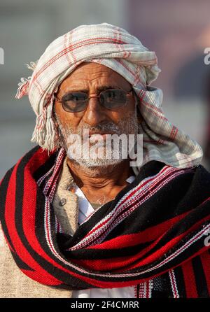 Homme dans un foulard avec châle rouge et noir regardant droit à moi. Il porte des lunettes de soleil, mais je sais qu'il me porte. Banque D'Images