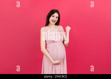 Jeune belle femme enceinte sur fond coloré isolé célébrant surpris et stupéfié pour le succès avec les bras levés et les yeux ouverts. Conc. Gagnant Banque D'Images