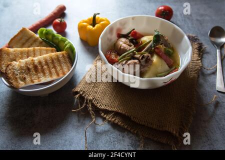 Gros plan du ragoût de poulet et des légumes dans un bol et condiments crus Banque D'Images