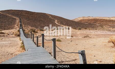 Une voie en plastique recyclé mène à la Menuiserie Aka HaMinsara dans le cratère de Makhtesh Ramon en Israël avec Mitzpe Ramon et un ciel bleu clair Banque D'Images