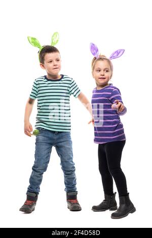 Joyeux et amusant, jeune garçon et petite fille tenant les mains en regardant loin avec le chapeau de lapin de Pâques. Corps entier isolé sur fond blanc Banque D'Images