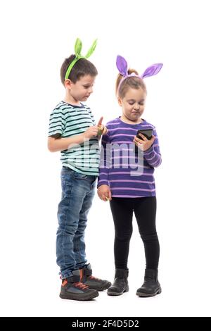 Les enfants de Pâques avec chapeau de lapin regardent et tiennent le smartphone à l'attention. Corps entier isolé sur fond blanc Banque D'Images